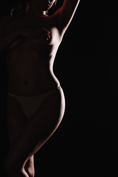 cropped view of woman covering breasts with hand while standing isolated on black  - Фото, зображення