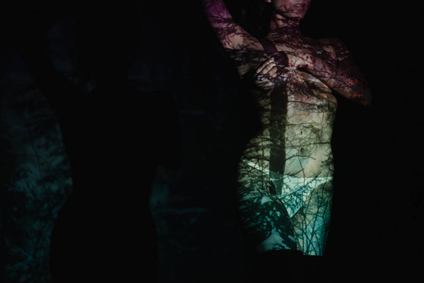 Ausgeschnittene Ansicht einer unbekleideten Frau mit Schatten und Licht am Körper, die auf schwarz steht  - Foto, Bild