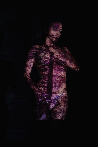 красива молода жінка з тінями на тілі, що покриває груди, що стоять на чорному
  - Фото, зображення