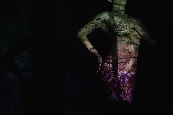 περικομμένη θέα της γδύθηκε νεαρή γυναίκα με σκιές στο σώμα, ενώ στέκεται στο μαύρο  - Φωτογραφία, εικόνα