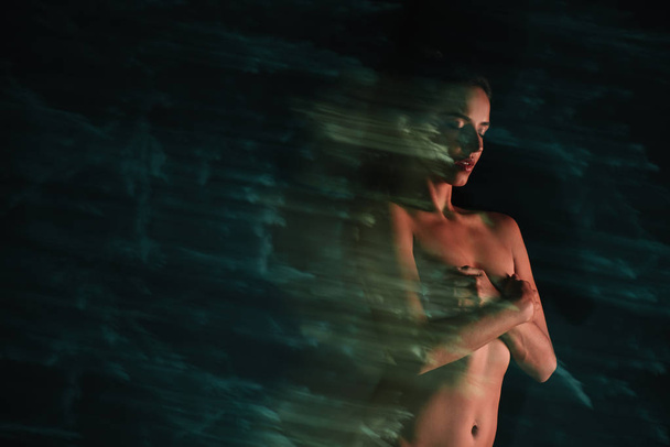 long exposure of naked girl standing and covering breasts on black  - Foto, Imagem