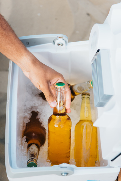 oříznutý pohled mladého muže s lahví piva z přenosné ledničky - Fotografie, Obrázek