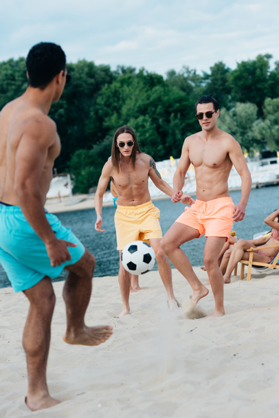 handsome, young multicultural men playing football on beach - Foto, afbeelding