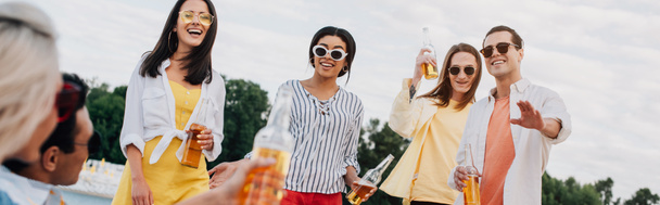 colpo panoramico di allegri amici multiculturali con bottiglie di birra che si divertono sulla spiaggia
 - Foto, immagini