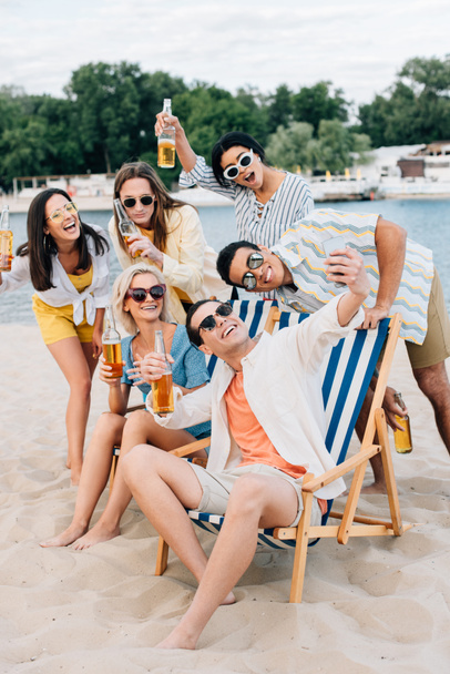 alegres amigos multiculturales tomando selfie mientras se divierten en la playa
 - Foto, Imagen