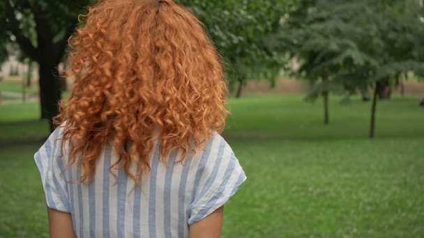 kıvırcık kızıl saçlı kız parkta yürüyüş seçici odak  - Video, Çekim