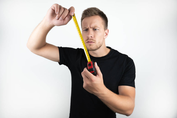 handsome young man wearing black t-shirt holding tape on isolated white background - Foto, Imagem