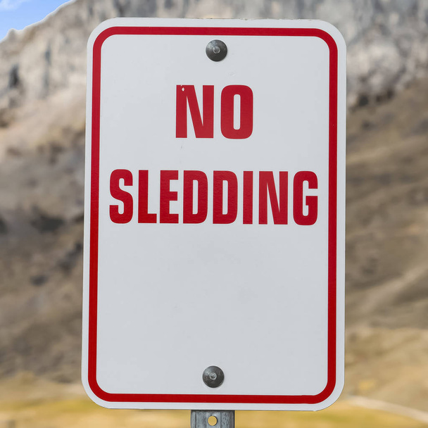 Close up de um sinal No Sledding com uma montanha imponente no fundo
 - Foto, Imagem