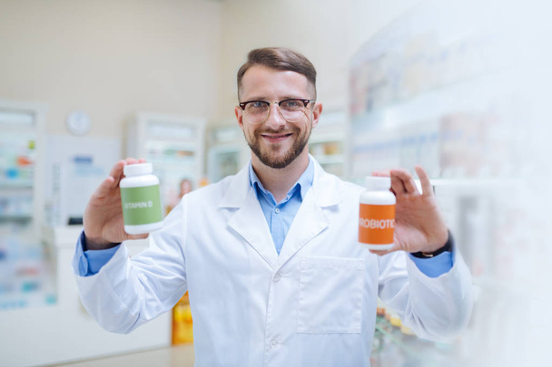 Cheerful young bearded apothecary giving useful recommendations - Foto, Bild