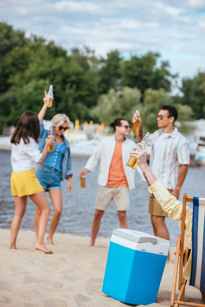 selektywne skupienie wesoły wielokulturowych przyjaciół posiadających butelki piwa podczas zabawy na plaży - Zdjęcie, obraz