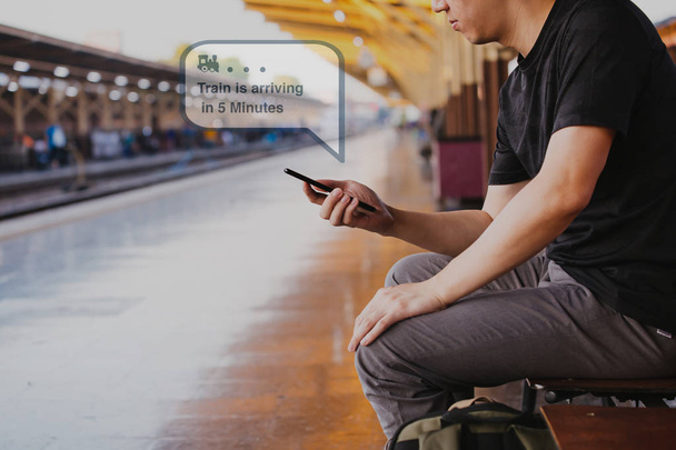Young male tourist backpacker use a phone and wait for public transportation inside train platform - Fotografie, Obrázek
