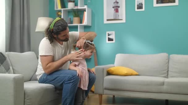 若いあごひげの父親は、彼の小さな女の子の髪をブラッシングし、尾を作ります - 映像、動画