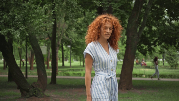 公園を歩く巻き毛の赤毛の女性の選択的な焦点  - 映像、動画