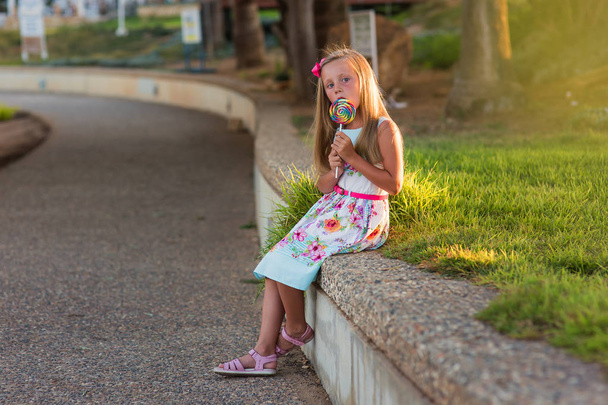 Portrait of a smiling girl with a lollipop at sunset in summer - Фото, изображение