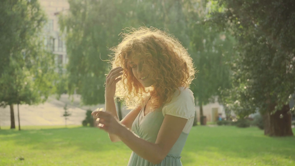 ευτυχισμένο σγουρά κορίτσι αγγίζοντας τα κόκκινα μαλλιά στο καλοκαίρι  - Πλάνα, βίντεο