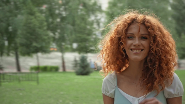 selective focus of beautiful curly girl smiling in park  - Materiał filmowy, wideo