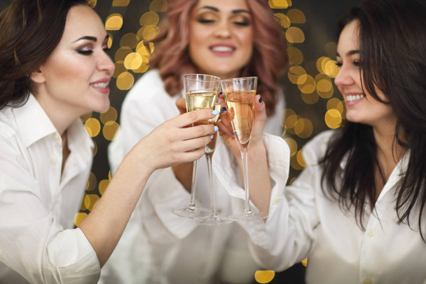 Mujeres sonrientes en mierdas blancas con copas de champán sobre ligh
 - Foto, Imagen