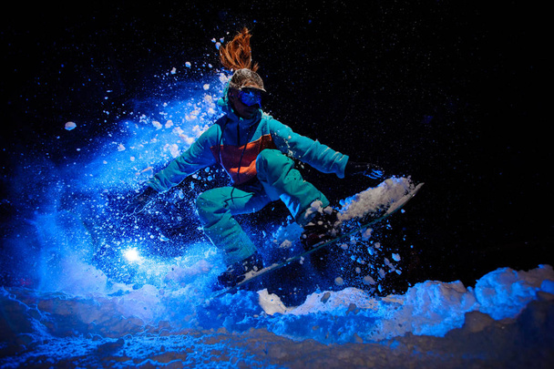 Female snowboarder dressed in a orange and blue sportswear performing tricks on the snow - Valokuva, kuva