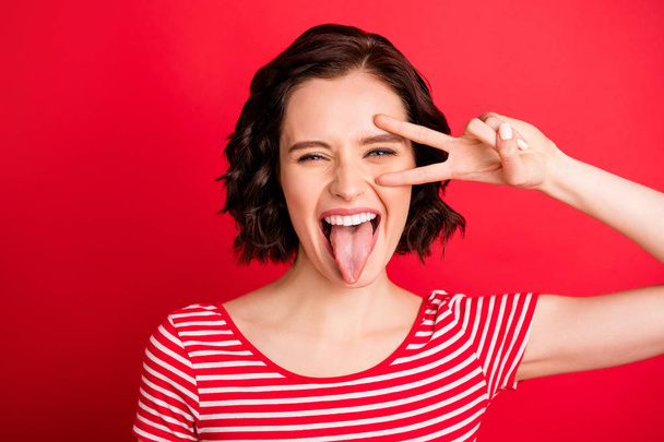 Photo of screaming girl showing her tongue after having eaten hot sauce while isolated with red background - Foto, afbeelding