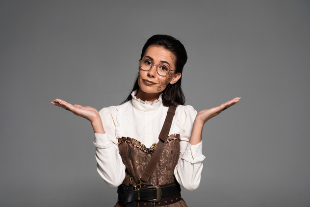 confused steampunk woman in glasses showing dubium gesture isolated on grey - Φωτογραφία, εικόνα