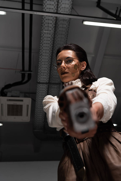selective focus of confident steampunk woman aiming with pistol at camera - Photo, Image