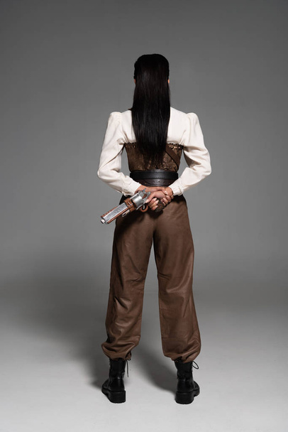 Вид женщины в полный рост, держащей винтажный пистолет на сером фоне
 - Фото, изображение