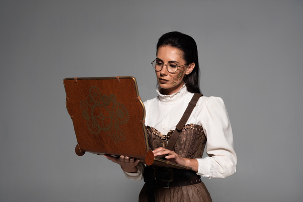 focused steampunk woman using vintage laptop isolated on grey - Photo, Image