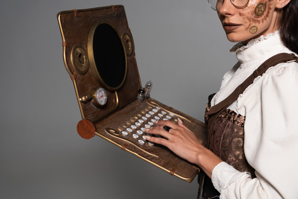 vue recadrée de la femme steampunk en utilisant un ordinateur portable vintage isolé sur gris
 - Photo, image