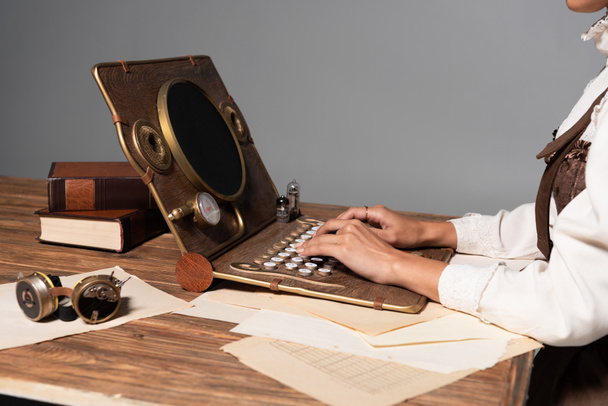 cropped view of woman typing on steampunk laptop at table isolated on grey - Photo, Image