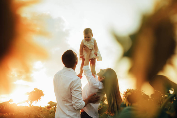 Šťastná rodina s dítětem se baví a hraje na slunečnicovém poli. - Fotografie, Obrázek