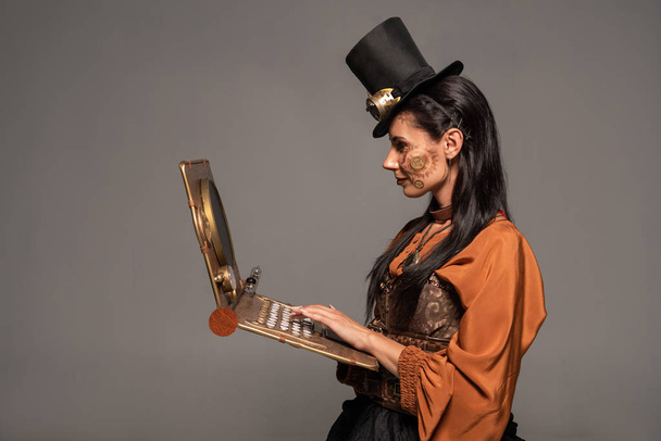 woman in top hat with goggles using steampunk laptop isolated on grey - Photo, Image