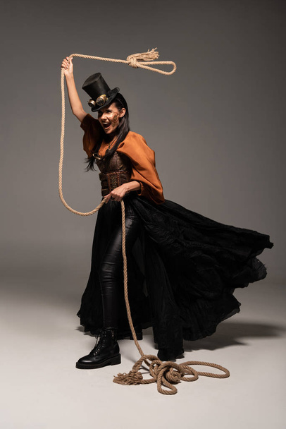 full length view of beautiful screaming steampunk woman holding lasso on grey - Foto, imagen