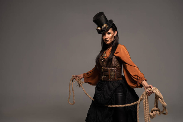 attractive steampunk girl in top hat holding lasso isolated on grey - Zdjęcie, obraz