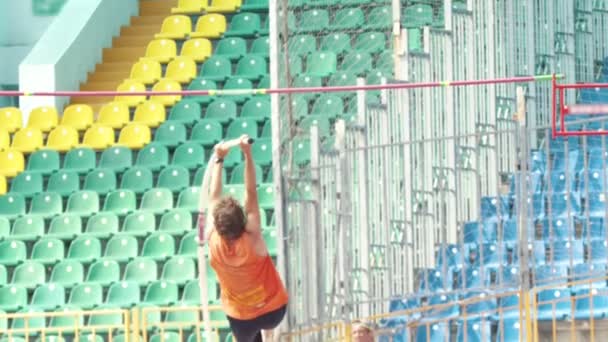 Pole vault - a man in orange shirt jumps over the bar - Materiał filmowy, wideo