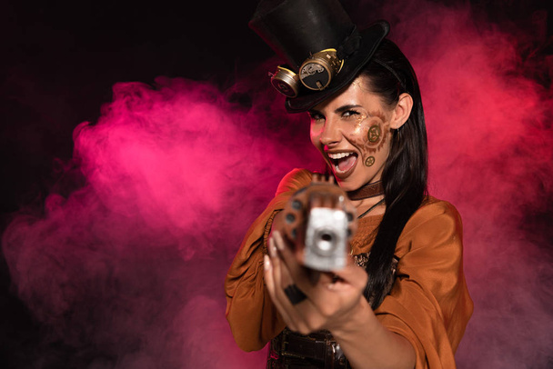 screaming steampunk woman aiming with pistol to camera in pink smoke on black - Foto, immagini
