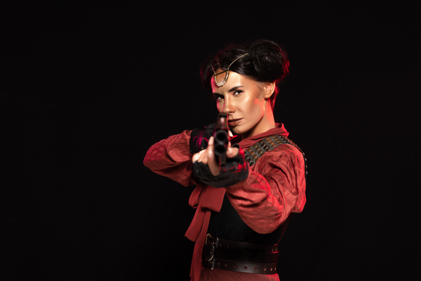 selective focus of steampunk woman aiming with gun to camera isolated on black - Foto, imagen