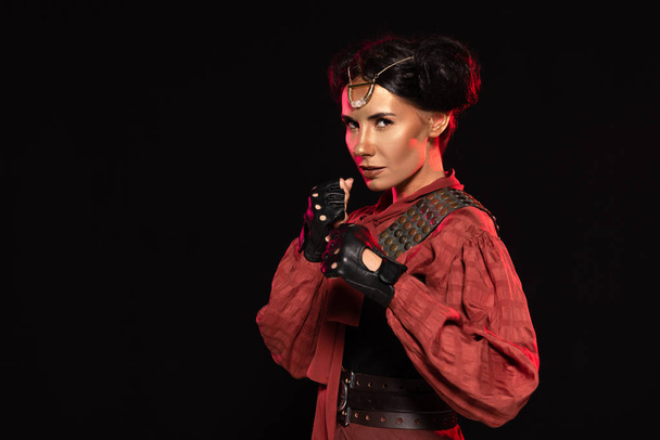 confident steampunk girl holding fists up and looking at camera isolated on black - Photo, Image