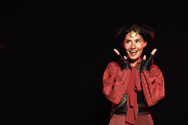 front view of attractive excited steampunk woman in leather gloves laughing isolated on black - Foto, imagen