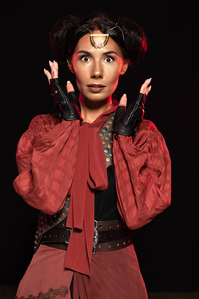 front view of attractive surprised steampunk woman in leather gloves isolated on black - Fotoğraf, Görsel