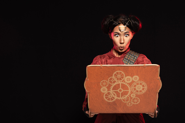 front view of attractive shocked steampunk woman using laptop isolated on black - Photo, Image