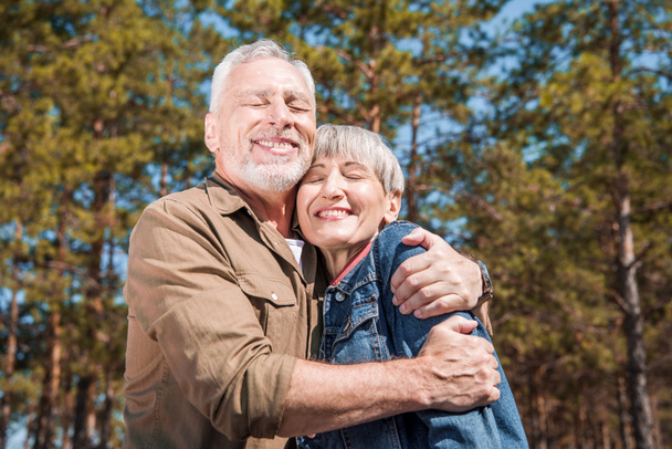 sonriente pareja de turistas mayores abrazando con los ojos cerrados en día soleado
 - Foto, imagen