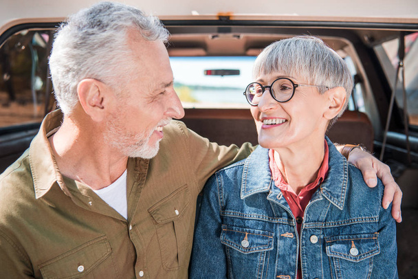 sonriendo pareja mayor abrazándose y mirándose el uno al otro cerca del coche
 - Foto, Imagen