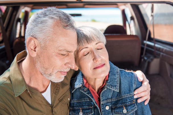 pareja mayor abrazando con los ojos cerrados cerca del coche
 - Foto, Imagen