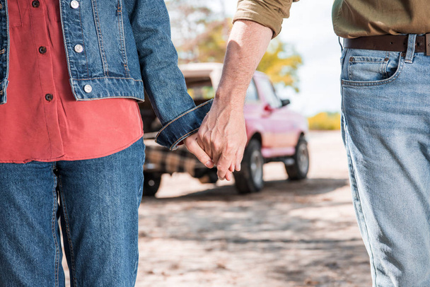 cropped view of senior couple holding hands near car in forest - Фото, изображение