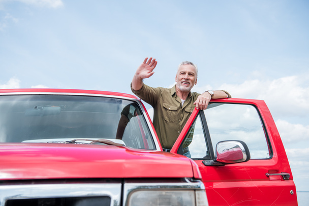 senior homme en chemise en voiture rouge agitant la main et souriant dans la journée ensoleillée
 - Photo, image