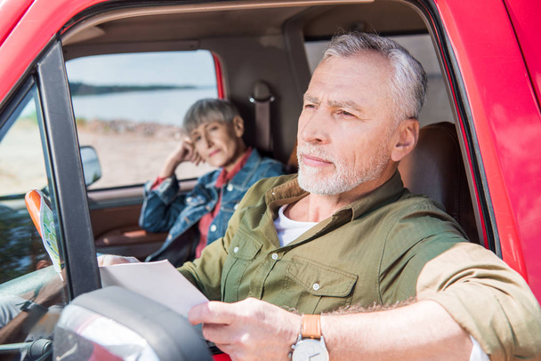 senior man holding map while sitting in car with wife - Photo, Image