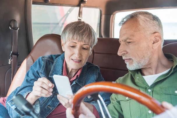 pareja de personas mayores utilizando el teléfono inteligente en coche en el día soleado
 - Foto, imagen