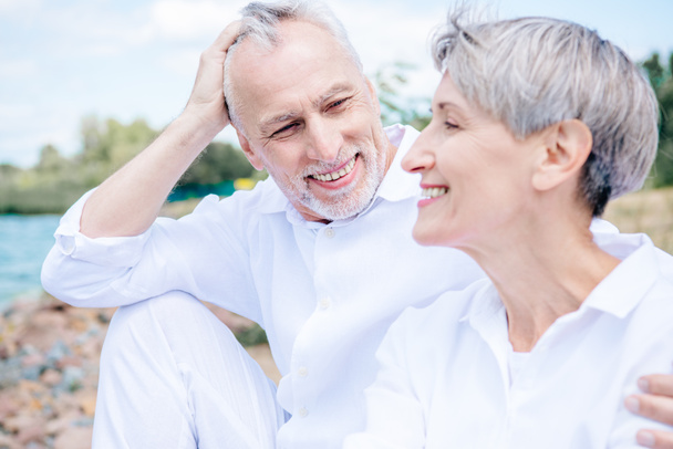 Gelukkig glimlachend Senior paar in witte shirts omarmen onder blauwe hemel - Foto, afbeelding