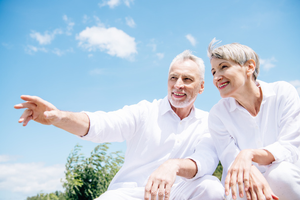 feliz sonriente pareja de ancianos en camisas blancas mirando hacia otro lado bajo el cielo azul
 - Foto, Imagen