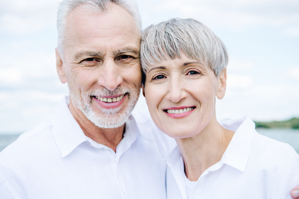 Вид улыбающейся счастливой пожилой пары в белых рубашках, смотрящей в камеру
 - Фото, изображение